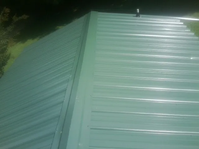 New green metal panels meeting at the ridge of a roof — Flat Roof Repair work by our crew in Otis