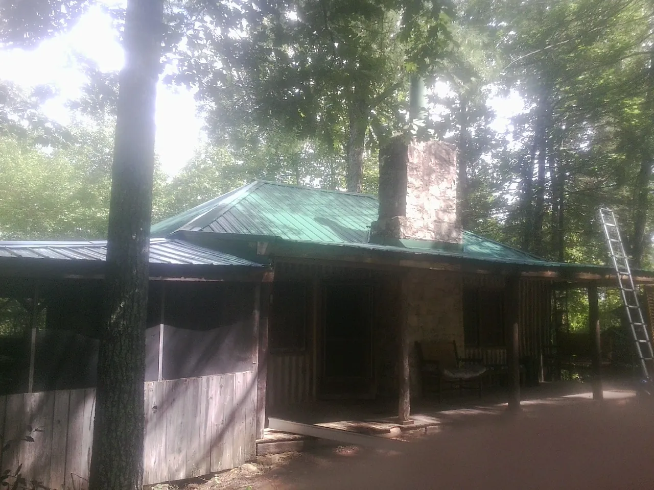 Green metal roof and stone chimney above a log cabin porch in Otis